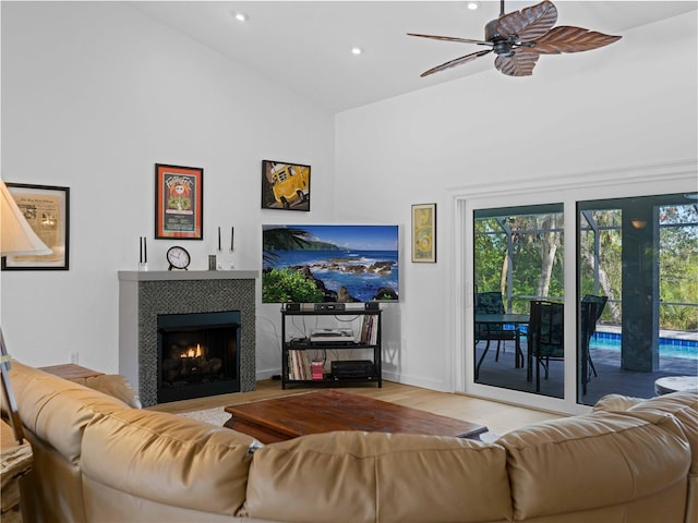 living room with high vaulted ceiling, wood-type flooring, a tiled fireplace, and ceiling fan