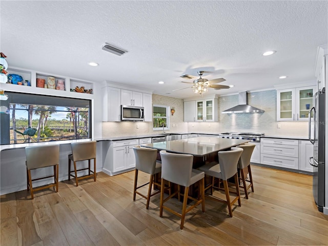 kitchen with white cabinets, appliances with stainless steel finishes, wall chimney exhaust hood, a kitchen island, and a breakfast bar area