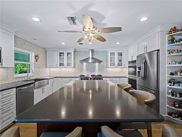 kitchen featuring white cabinetry, appliances with stainless steel finishes, a center island, wall chimney range hood, and sink