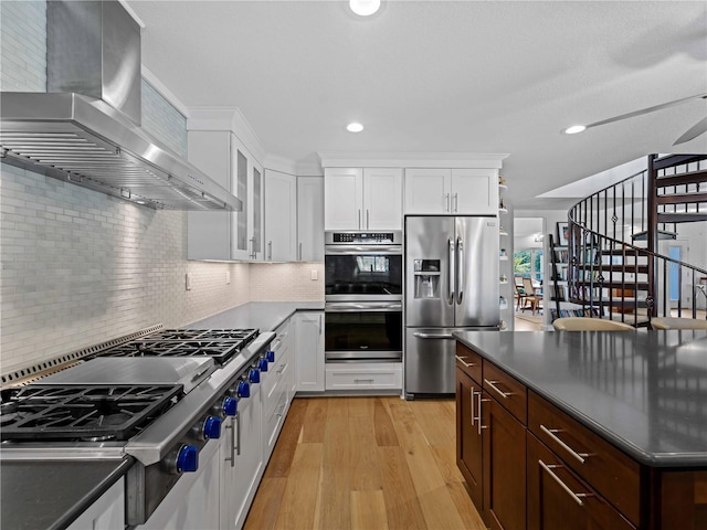 kitchen with appliances with stainless steel finishes, wall chimney exhaust hood, and white cabinets