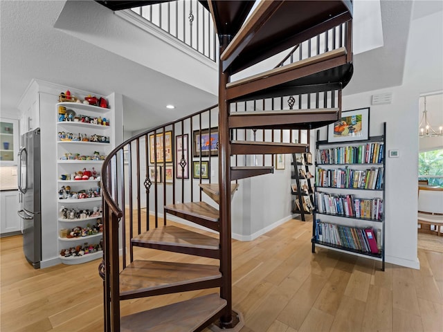 stairs featuring a high ceiling, an inviting chandelier, a textured ceiling, and hardwood / wood-style floors