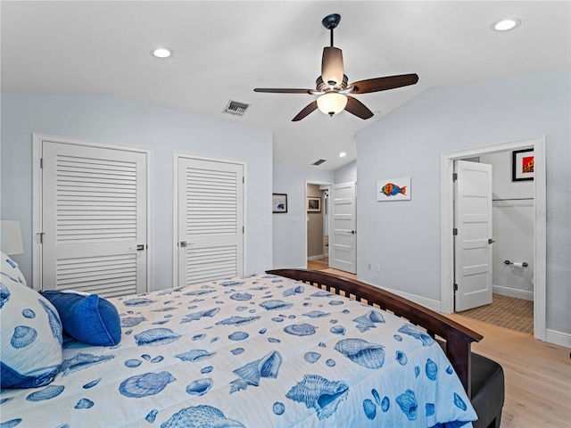 bedroom featuring ceiling fan, vaulted ceiling, two closets, and light hardwood / wood-style flooring