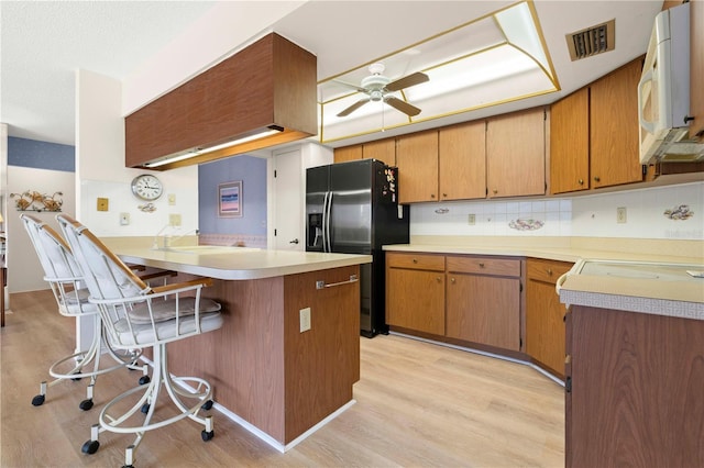 kitchen with ceiling fan, black refrigerator with ice dispenser, a kitchen bar, kitchen peninsula, and light hardwood / wood-style flooring