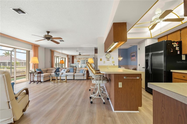 kitchen with a kitchen bar, kitchen peninsula, black fridge, light wood-type flooring, and a textured ceiling