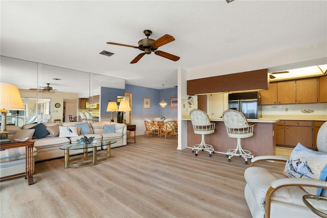 living room with ceiling fan, a textured ceiling, and light hardwood / wood-style floors