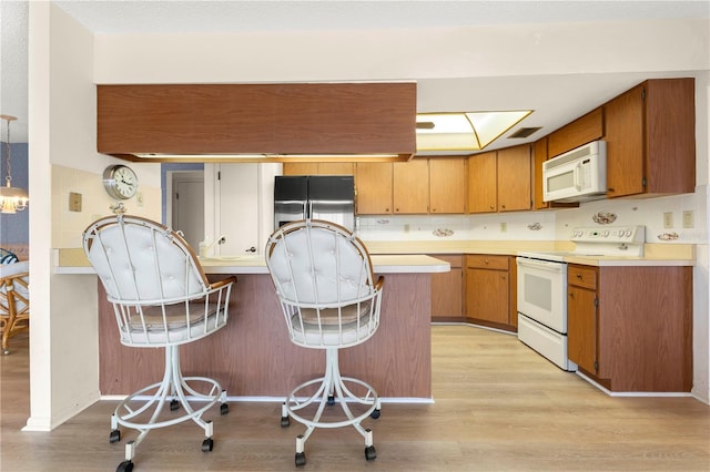 kitchen featuring white appliances, decorative light fixtures, kitchen peninsula, light hardwood / wood-style flooring, and a breakfast bar area