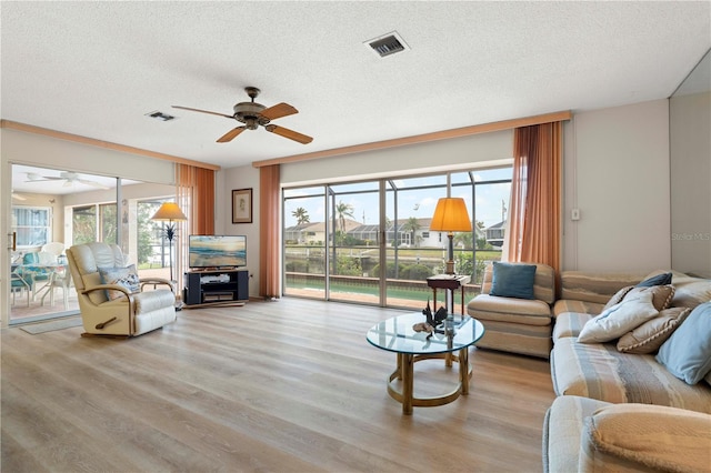 living room with a textured ceiling, ceiling fan, and light hardwood / wood-style flooring