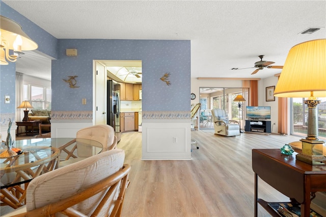 living room with ceiling fan, a textured ceiling, and light wood-type flooring