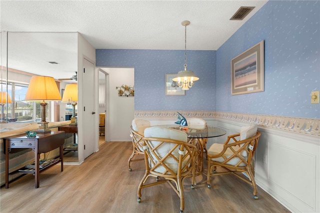 dining area with a textured ceiling, ceiling fan with notable chandelier, and hardwood / wood-style floors