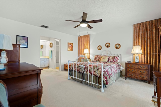 bedroom with light carpet, ceiling fan, a textured ceiling, and ensuite bath