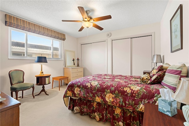 bedroom featuring ceiling fan, light carpet, multiple closets, and a textured ceiling