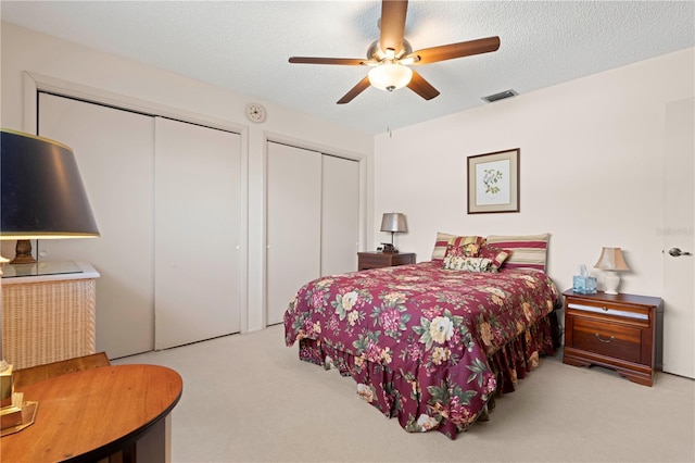 bedroom with ceiling fan, multiple closets, light carpet, and a textured ceiling