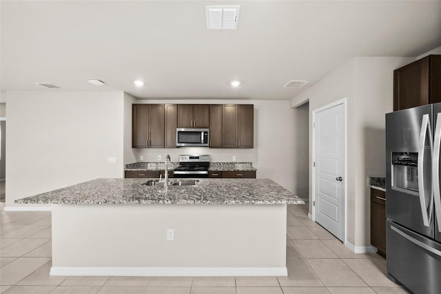 kitchen featuring sink, light stone countertops, an island with sink, and stainless steel appliances