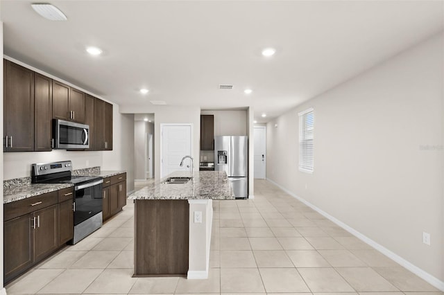 kitchen with sink, dark brown cabinetry, a kitchen island with sink, light stone countertops, and appliances with stainless steel finishes