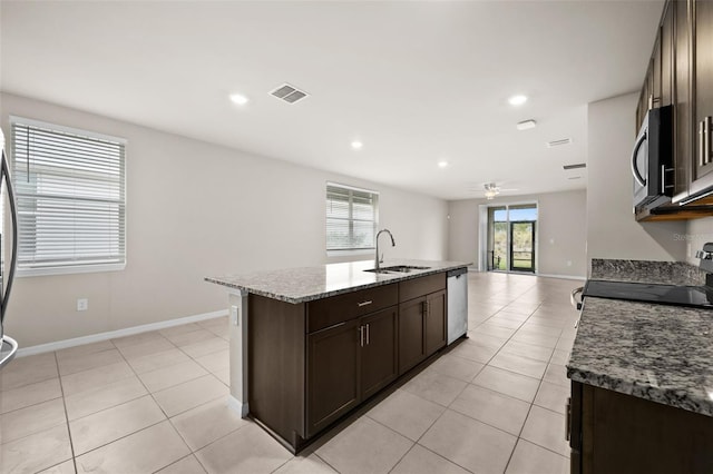 kitchen with light stone countertops, appliances with stainless steel finishes, an island with sink, sink, and ceiling fan