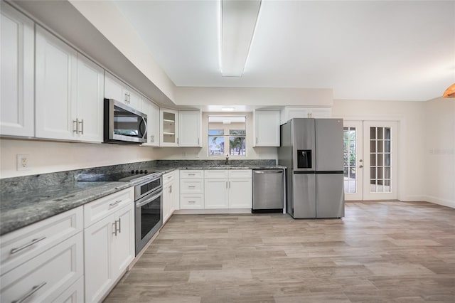 kitchen with appliances with stainless steel finishes, white cabinetry, french doors, dark stone counters, and light wood-type flooring