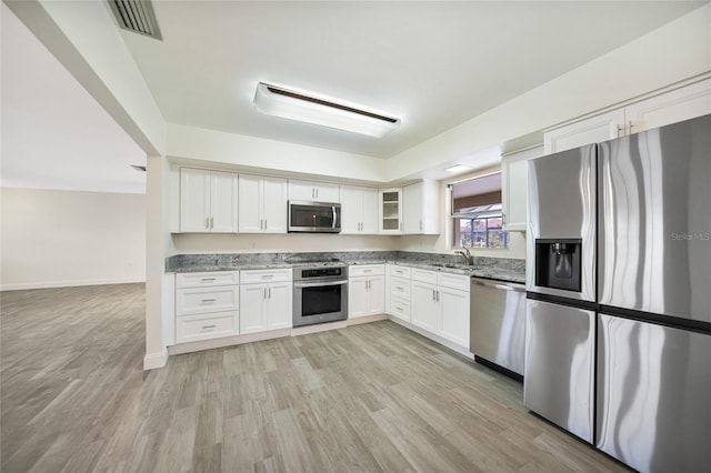 kitchen with appliances with stainless steel finishes, white cabinetry, sink, light stone countertops, and light wood-type flooring