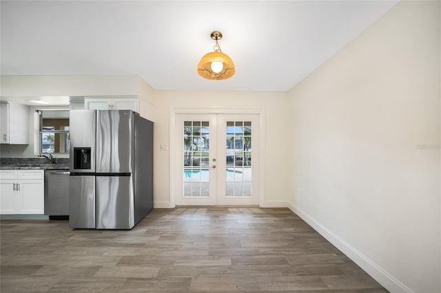 kitchen with appliances with stainless steel finishes, hardwood / wood-style floors, white cabinetry, sink, and french doors