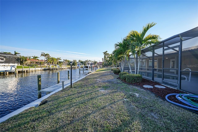 dock area featuring a water view, glass enclosure, and a lawn