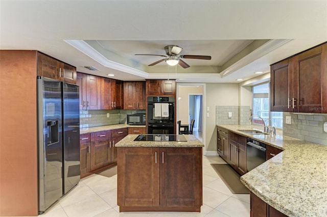 kitchen featuring light stone counters, a tray ceiling, black appliances, and a kitchen island