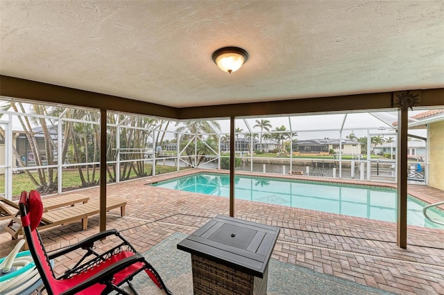 view of pool with a water view, glass enclosure, and a patio area