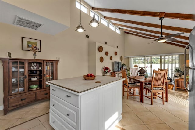 kitchen featuring decorative light fixtures, white cabinetry, beam ceiling, light tile patterned flooring, and a kitchen island