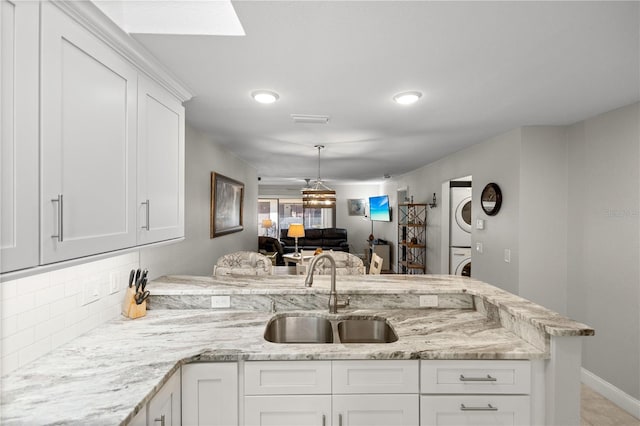 kitchen featuring white cabinetry, sink, stacked washer and clothes dryer, and kitchen peninsula