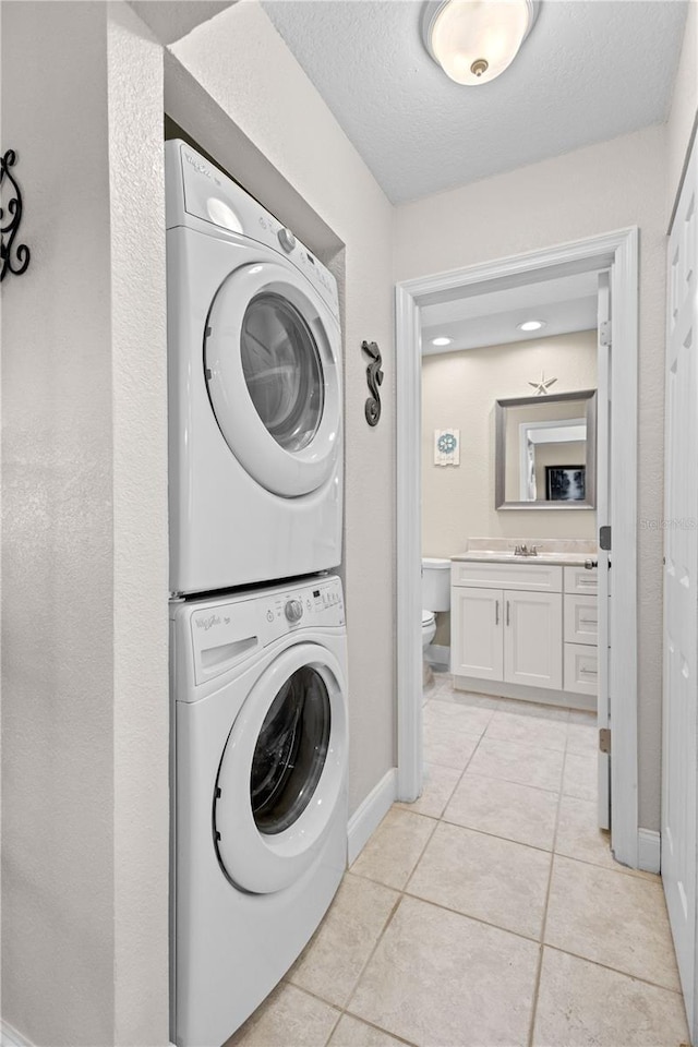 laundry room featuring sink, light tile patterned flooring, a textured ceiling, and stacked washing maching and dryer