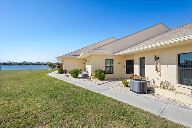 rear view of house featuring central AC unit, a lawn, and a water view