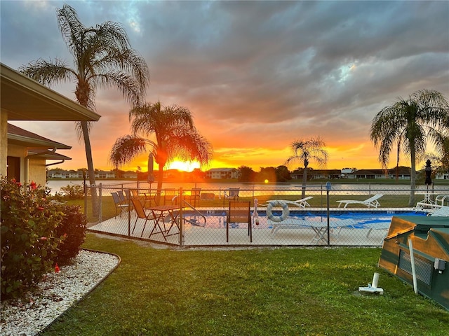 pool at dusk with a water view and a yard