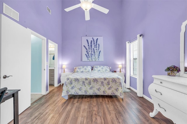 bedroom featuring wood-type flooring, a towering ceiling, connected bathroom, and ceiling fan