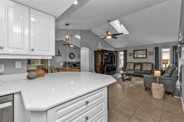 kitchen with white cabinets, kitchen peninsula, ceiling fan, light tile patterned floors, and lofted ceiling with skylight