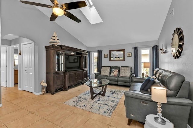 living room with ceiling fan, vaulted ceiling with skylight, and light tile patterned flooring