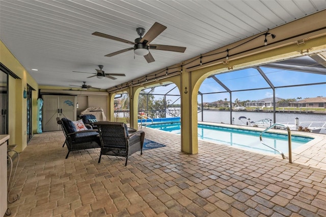 view of swimming pool featuring ceiling fan, a lanai, a water view, and a patio