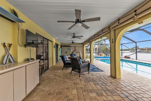 view of patio with ceiling fan, a lanai, and a water view