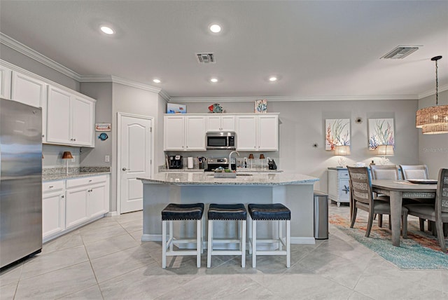 kitchen with a kitchen island with sink, white cabinets, stainless steel appliances, and pendant lighting