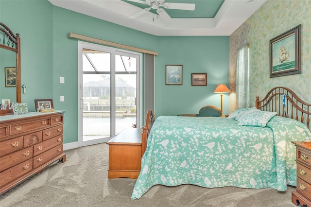 carpeted bedroom featuring access to exterior, ceiling fan, and a tray ceiling