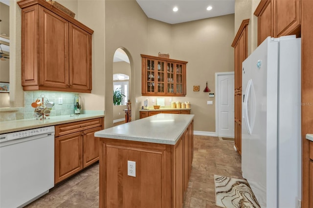 kitchen featuring tasteful backsplash, white appliances, a center island, and a towering ceiling