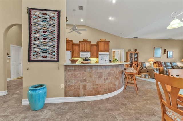 kitchen with a kitchen bar, white appliances, vaulted ceiling, kitchen peninsula, and ceiling fan