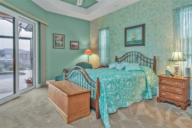 carpeted bedroom with access to exterior and a tray ceiling