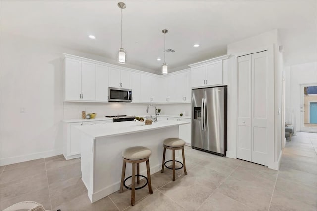 kitchen with a breakfast bar, appliances with stainless steel finishes, white cabinetry, a center island with sink, and decorative light fixtures