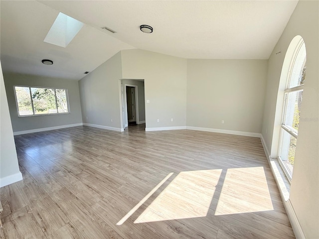 empty room featuring light wood-style floors, visible vents, baseboards, and lofted ceiling with skylight