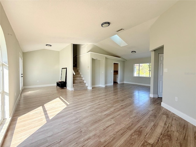 unfurnished living room featuring vaulted ceiling with skylight, light wood-style flooring, stairs, and visible vents