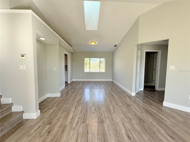 unfurnished room featuring lofted ceiling with skylight, stairway, baseboards, and wood finished floors