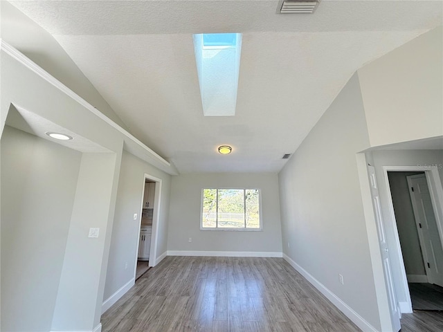 empty room with baseboards, visible vents, lofted ceiling with skylight, a textured ceiling, and light wood-style floors