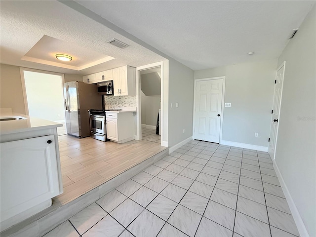 kitchen featuring white cabinets, appliances with stainless steel finishes, a tray ceiling, light countertops, and backsplash