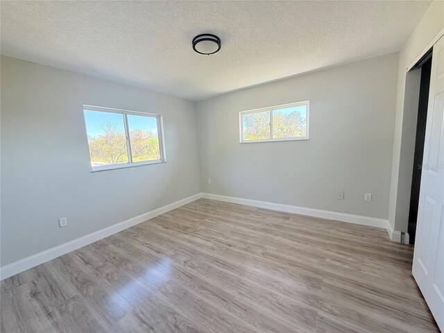 unfurnished room featuring a textured ceiling, light wood finished floors, and baseboards