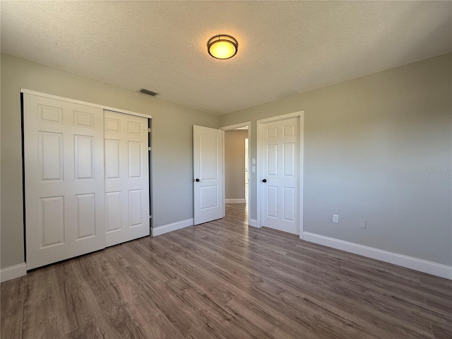 unfurnished bedroom featuring dark wood-style floors, a closet, visible vents, and baseboards