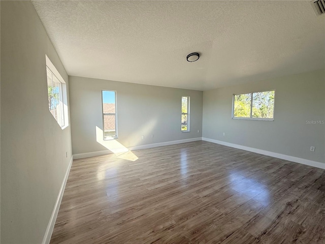 spare room featuring baseboards, a textured ceiling, visible vents, and wood finished floors