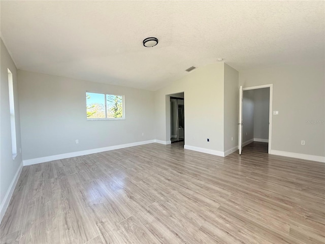 unfurnished room with a textured ceiling, light wood finished floors, visible vents, and baseboards